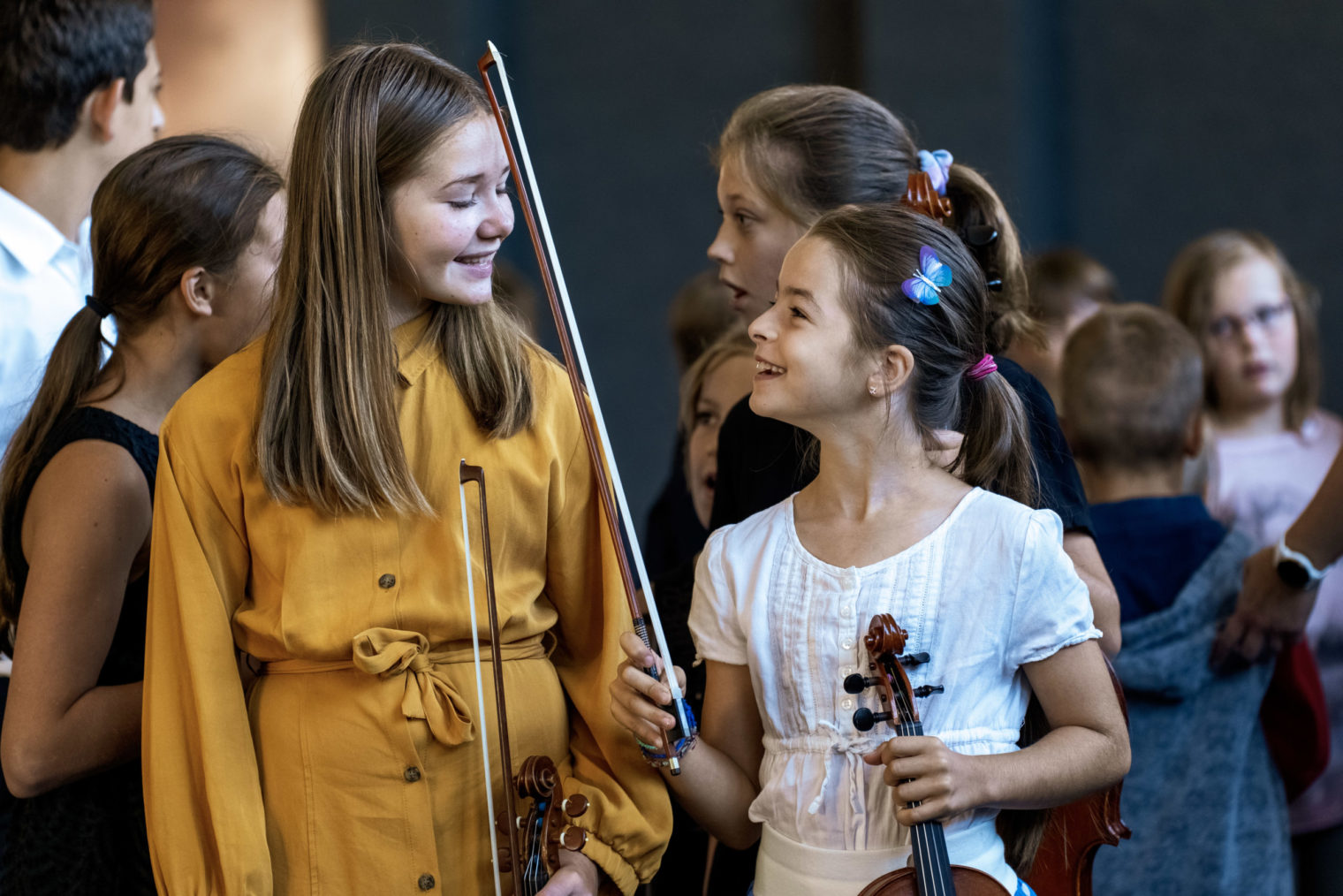 Zwei Mädchen des Jugendstreichorchesters lachen einander an, ein Mädchen hält dabei Geige und Bogen in den Händen