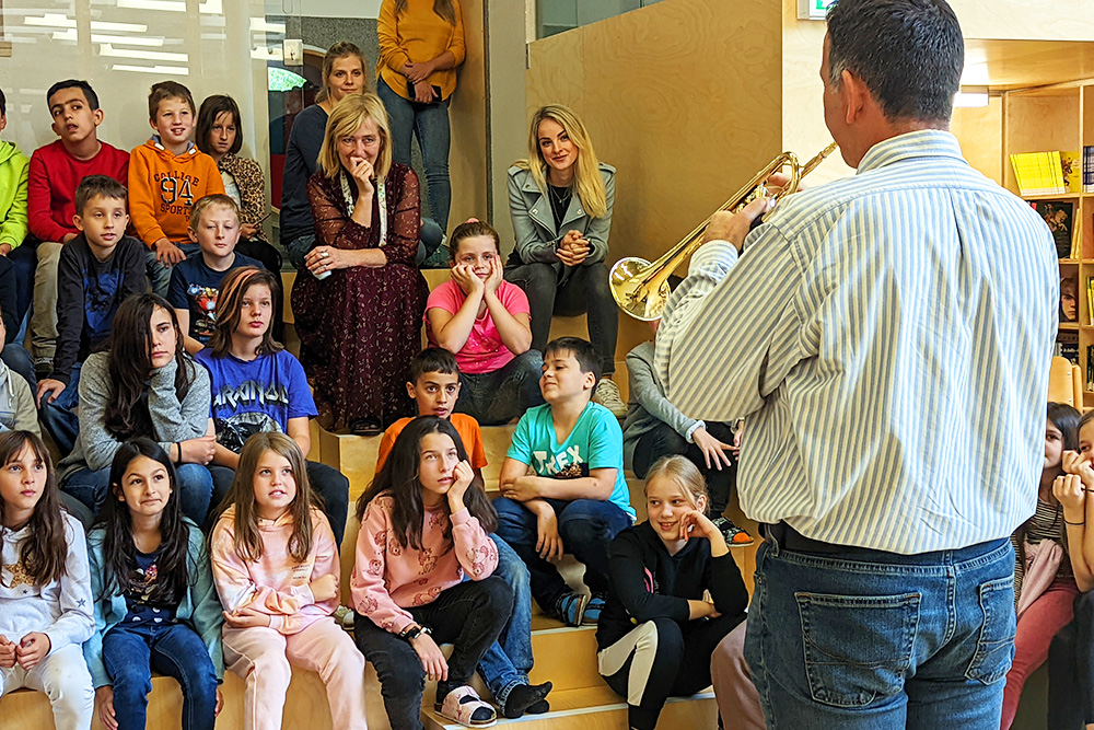 Ein Publikum von Volksschüler:innen hört beim Trompetespielen zu