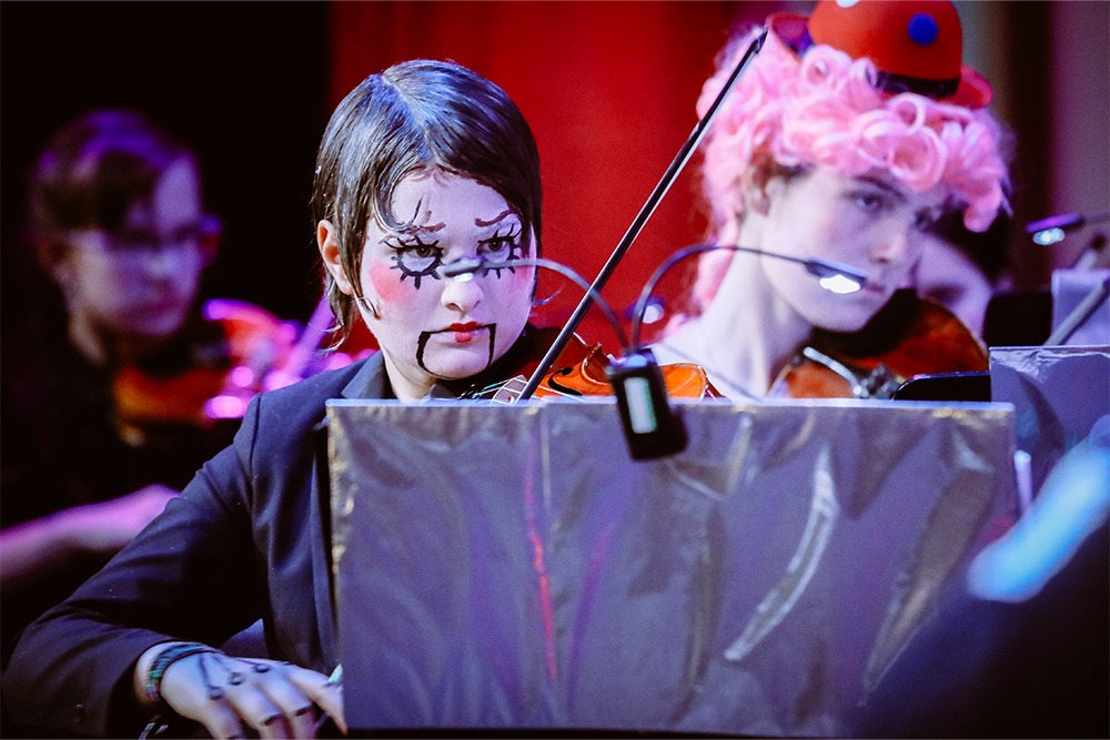 Ein verkleidetes Musikschulkind mit Violinenbogen blickt konzentriert auf seine Noten